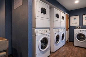 A laundry room with stacked front-loading washers and dryers, wooden flooring, and a blue wall. - King Bed 1BR Suite w/ Free Breakfast, Pool & Gym (Dublin)