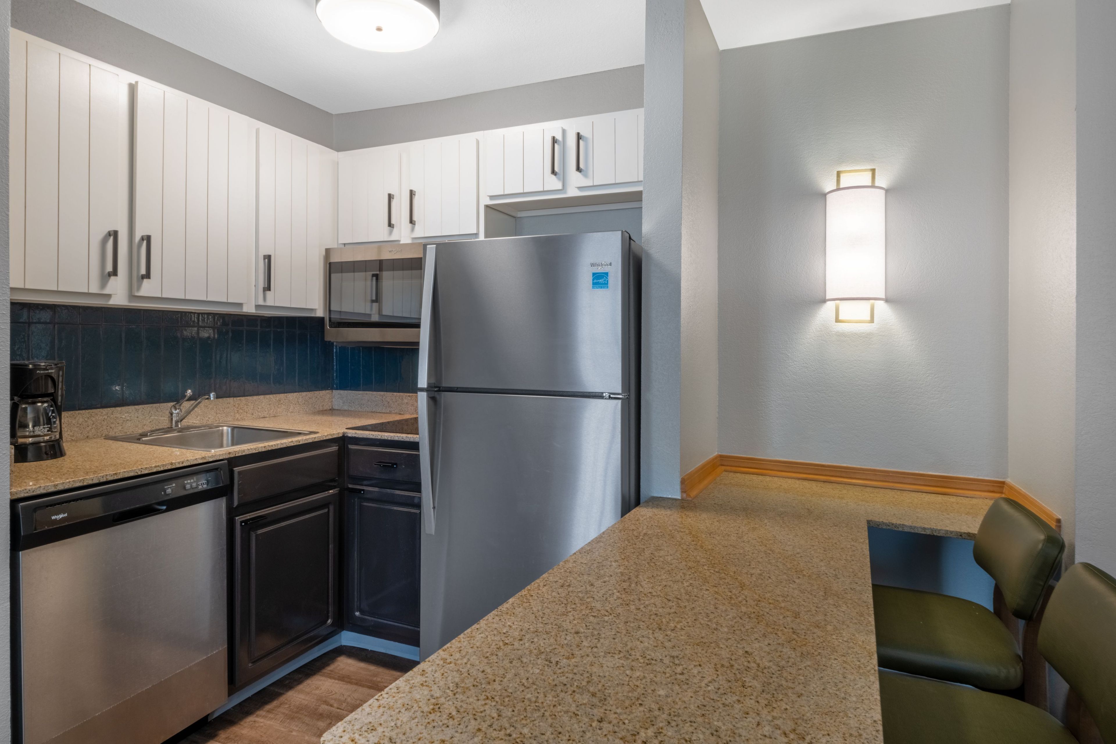 A compact kitchen with white cabinets, a stainless steel refrigerator, a dishwasher, and a built-in oven.