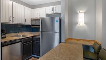 A compact kitchen with white cabinets, a stainless steel refrigerator, a dishwasher, and a built-in oven.