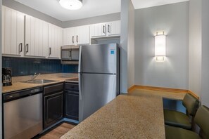 A compact kitchen with white cabinets, a stainless steel refrigerator, a dishwasher, and a built-in oven. - King Bed 1BR Suite w/ Free Breakfast, Pool & Gym (Dublin)