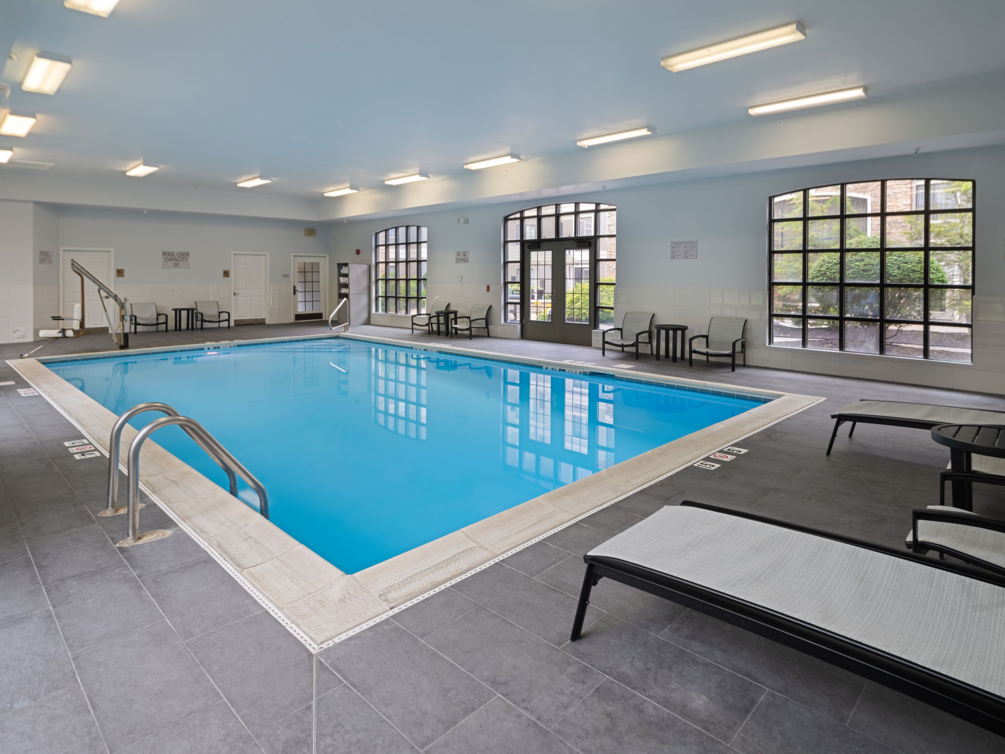 An indoor swimming pool with clear water, surrounded by lounge chairs and a tiled floor.