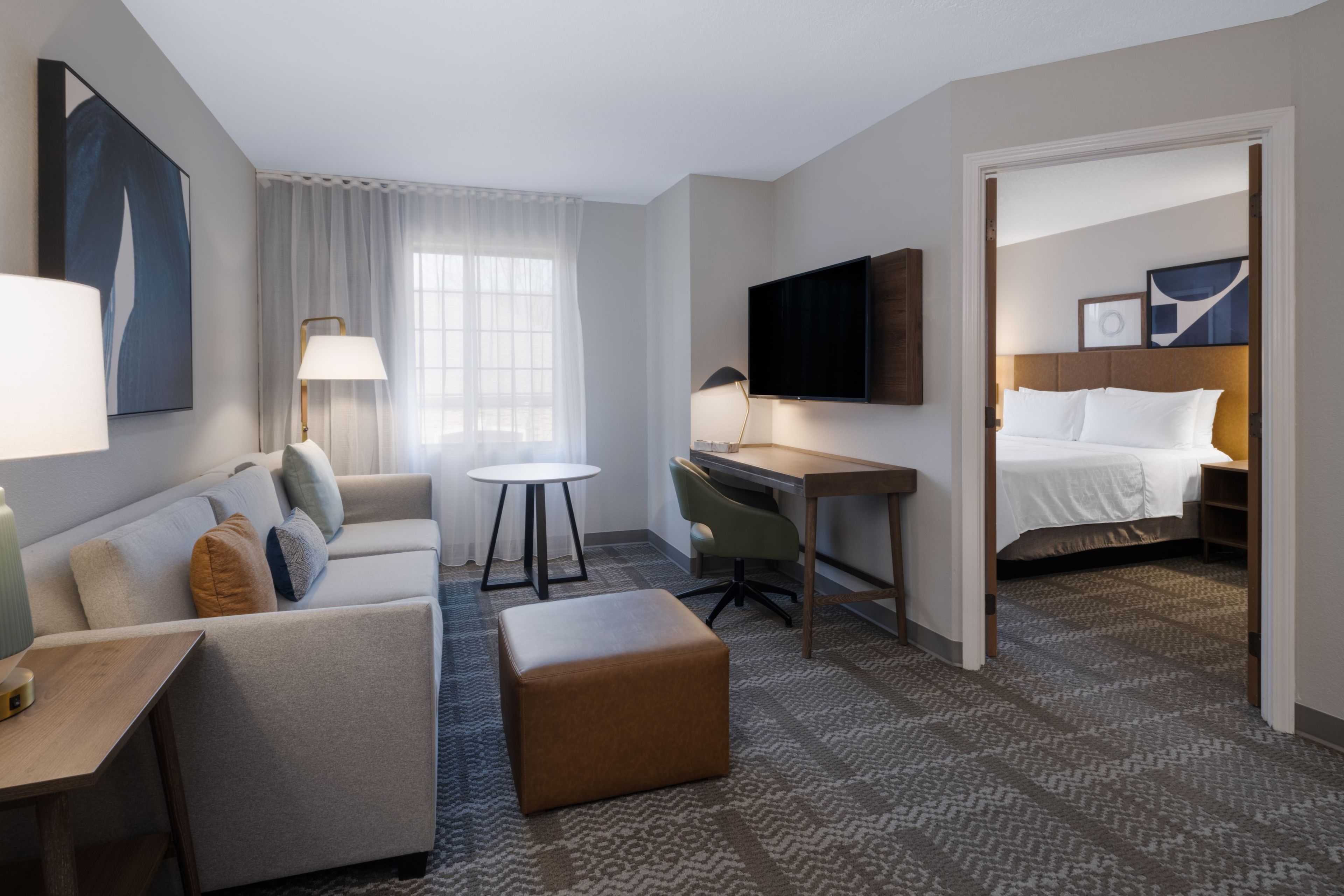 A hotel room with a bed, a desk, a chair, a sofa, a small table, and a television.