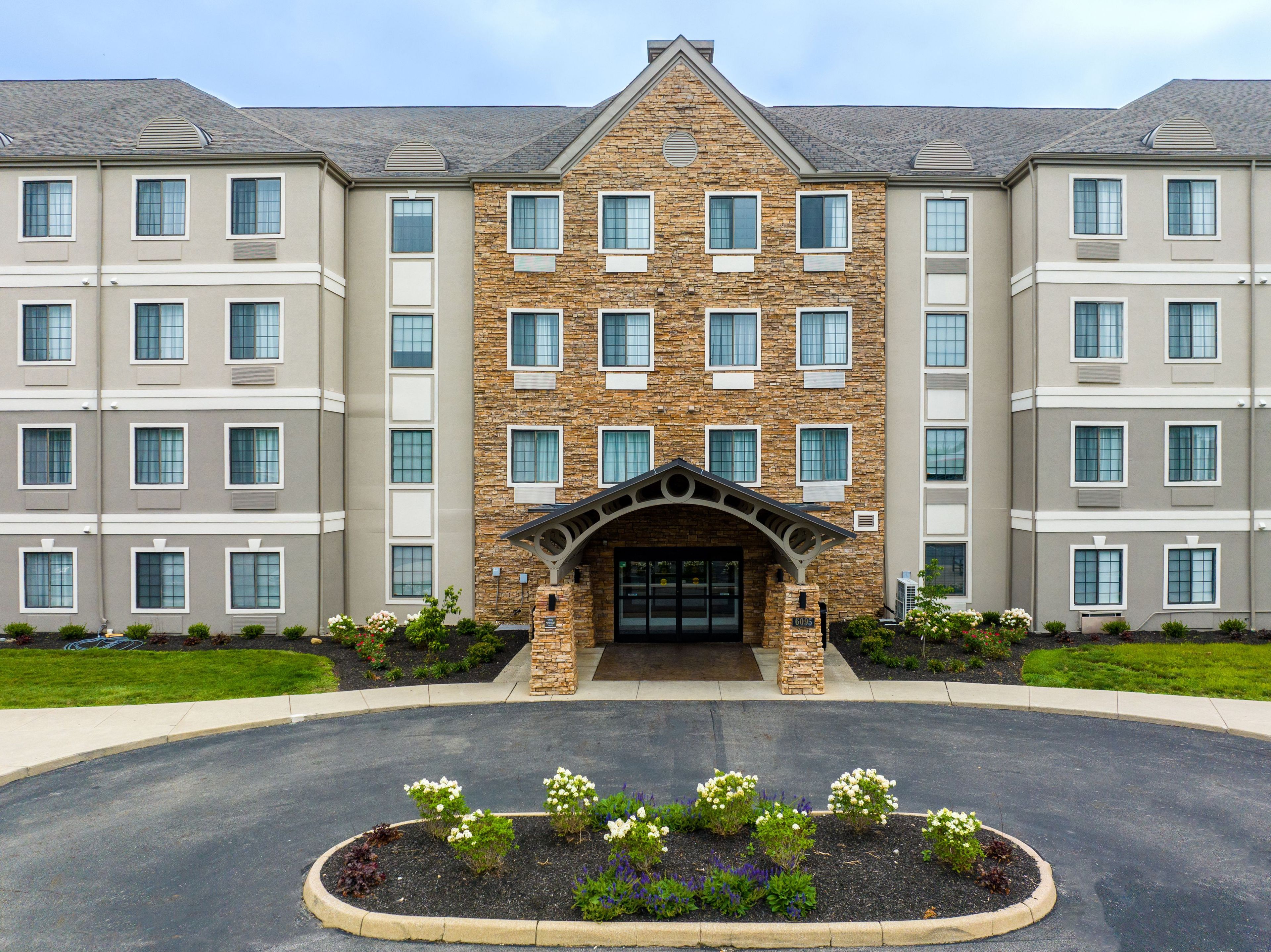 A multi-story hotel with a stone facade, a central entrance with a decorative arch, and a landscaped driveway.