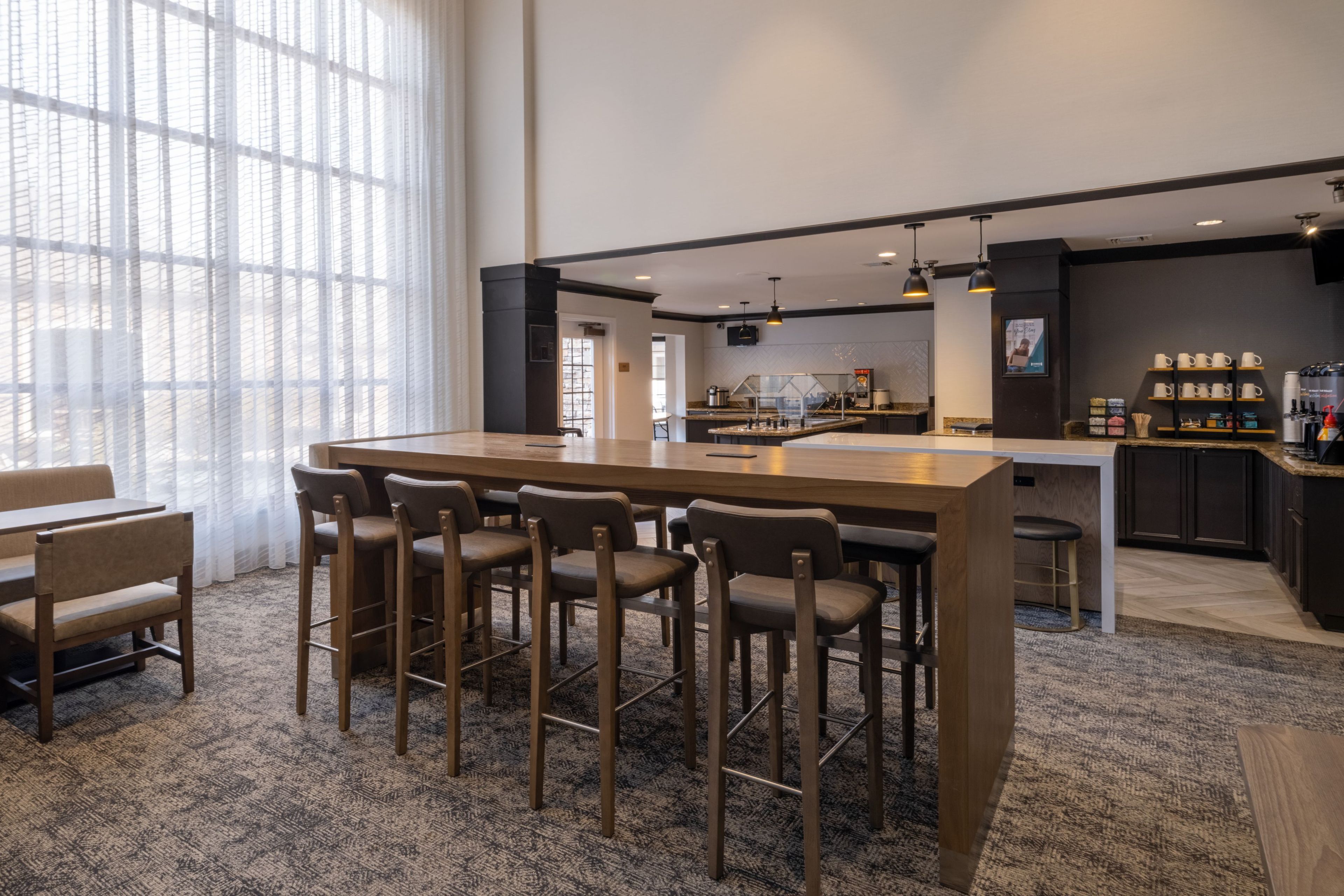 A modern bar area with a long counter, bar stools, and a seating area with tables and chairs.
