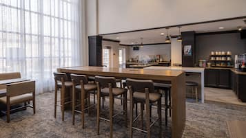 A modern bar area with a long counter, bar stools, and a seating area with tables and chairs.