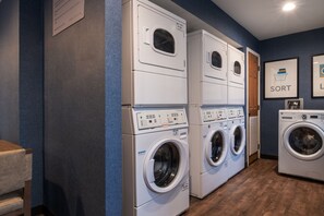 Une buanderie équipée de machines à laver et de sèche-linge à chargement frontal superposés, avec un plancher en bois et un mur bleu.
