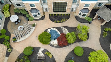 A rooftop garden with a circular seating area, a small fountain, and various plants.