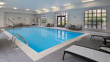 An indoor swimming pool with clear water, surrounded by lounge chairs and a tiled floor.