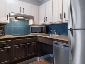 Una cocina moderna con armarios blancos, un refrigerador de acero inoxidable, un microondas y un lavavajillas.