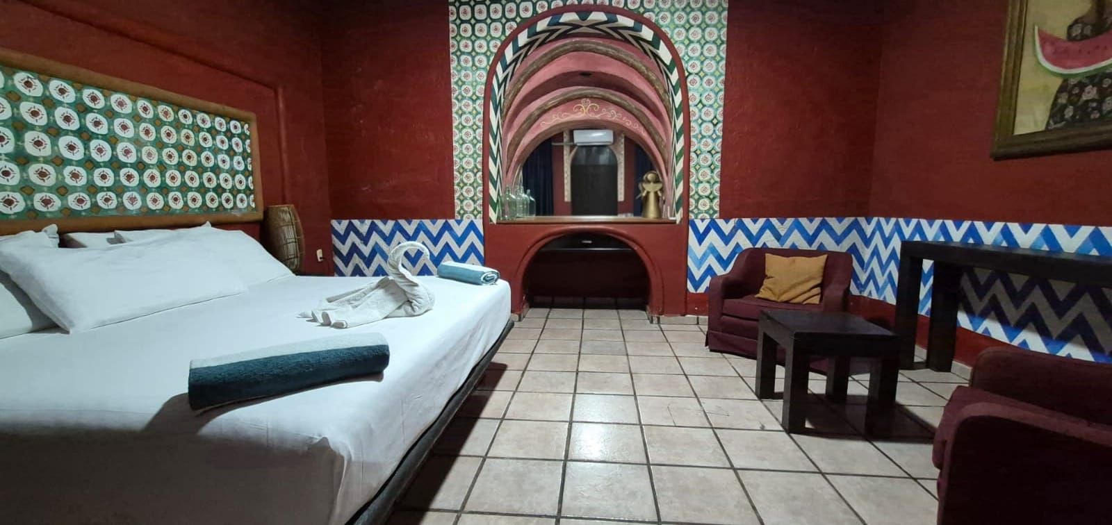 A hotel room with a bed, a sofa, a small table, and a decorative mirror.