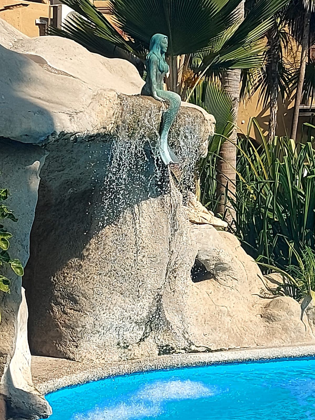 A statue of a mermaid sitting on a rock by a pool.