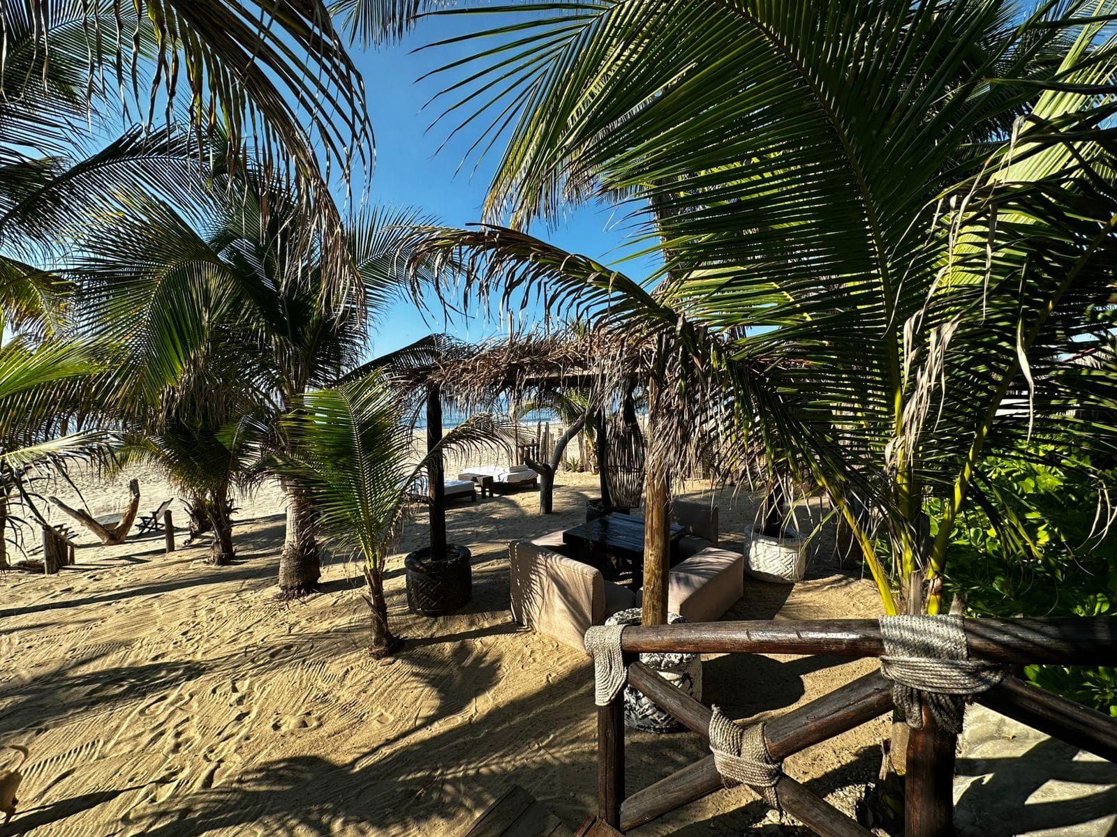 Un décor de plage avec des palmiers, des structures en bois et des chaises longues.