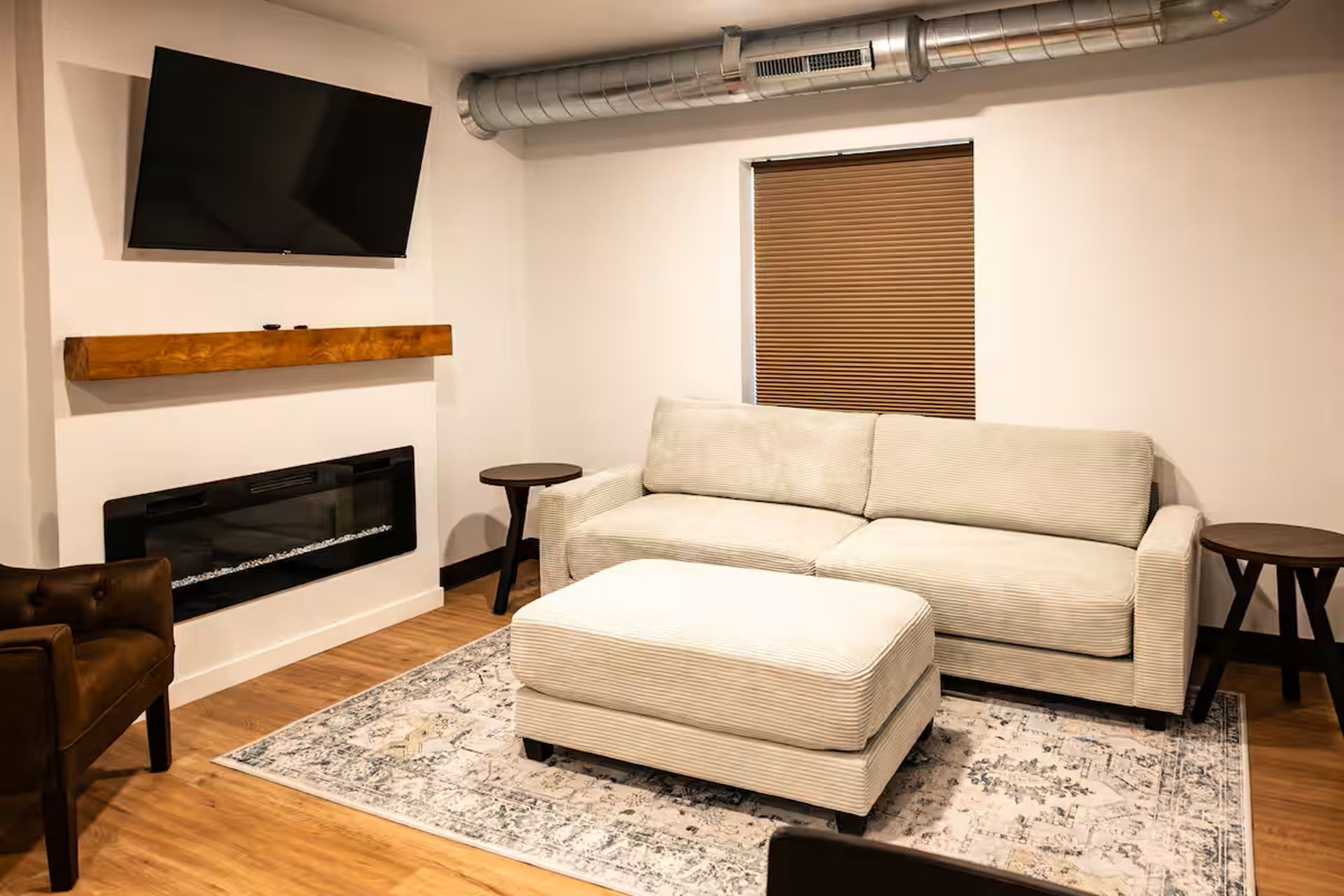 A living room with a sofa, ottoman, TV, fireplace, and a round table.