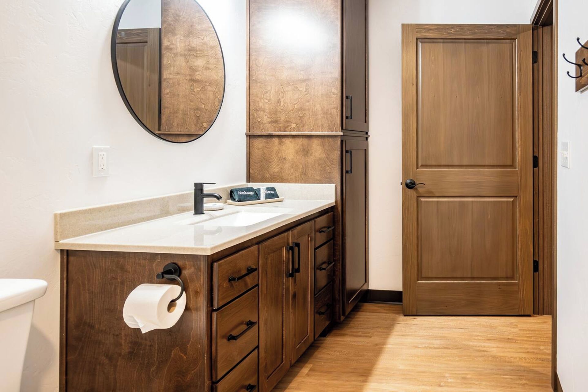Un baño con tocador de madera, un lavabo, un inodoro, un espejo y una puerta.