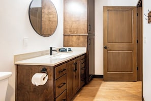 Un baño con tocador de madera, un lavabo, un inodoro, un espejo y una puerta.