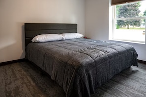 A single bed with a dark headboard and white pillows in a room with a large window. - Exclusive Full-Complex Retreat: Reserve All 7 Suites & Common Areas (Brillion)