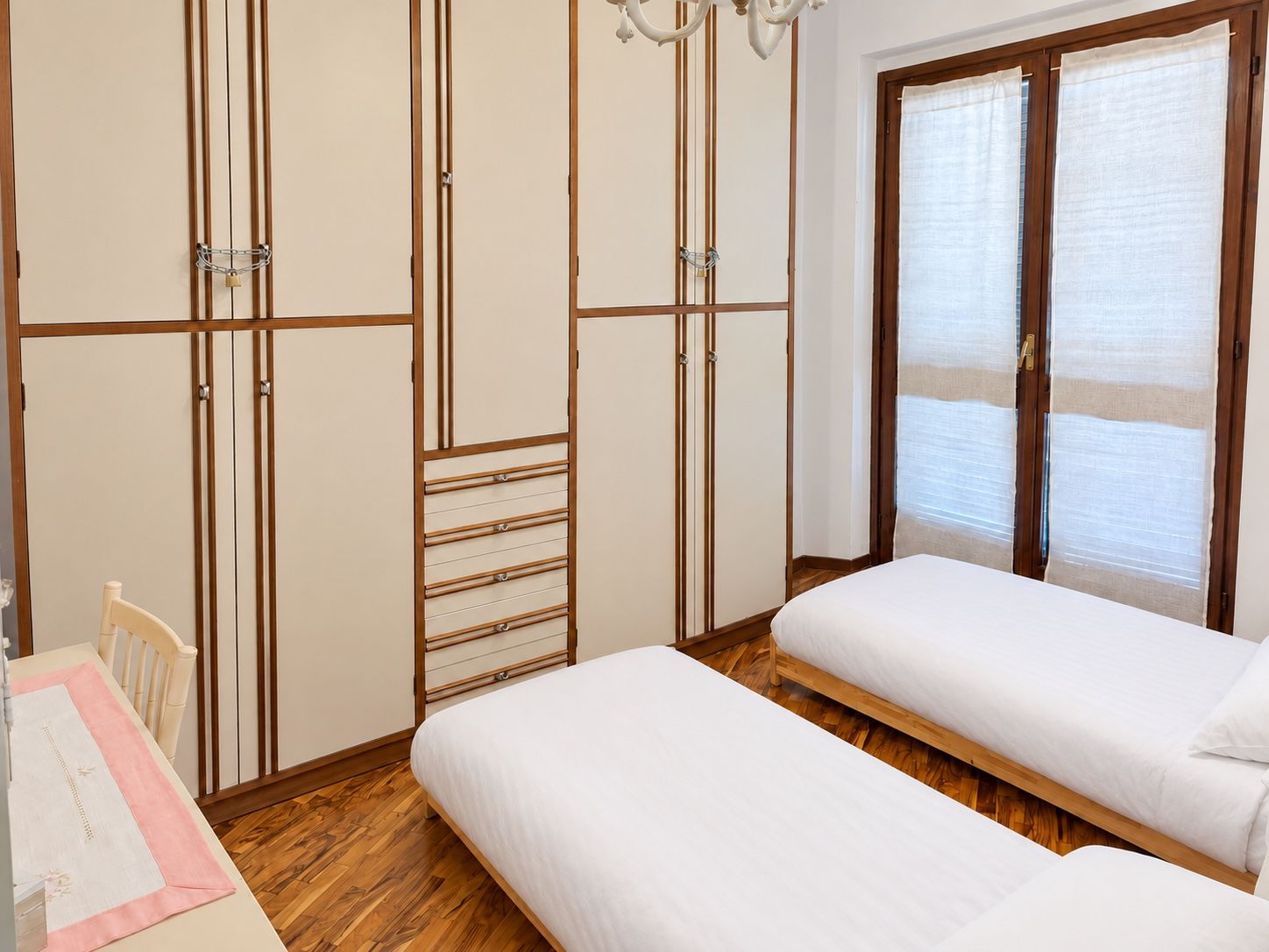 Ein Schlafzimmer mit zwei Einzelbetten, einem Holzschrank, einem Schreibtisch mit Stuhl und einem Fenster mit Jalousien.