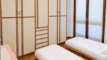 Ein Schlafzimmer mit zwei Einzelbetten, einem Holzschrank, einem Schreibtisch mit Stuhl und einem Fenster mit Jalousien.