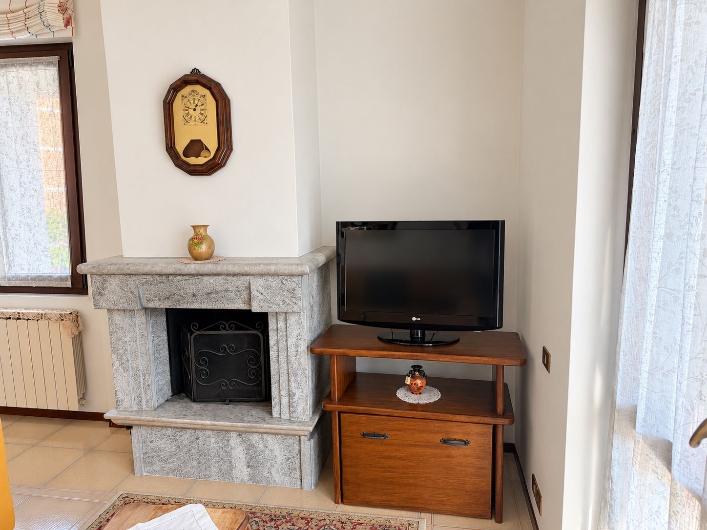 Un salon avec une cheminée, un téléviseur posé sur un meuble en bois et une horloge décorative accrochée au mur.