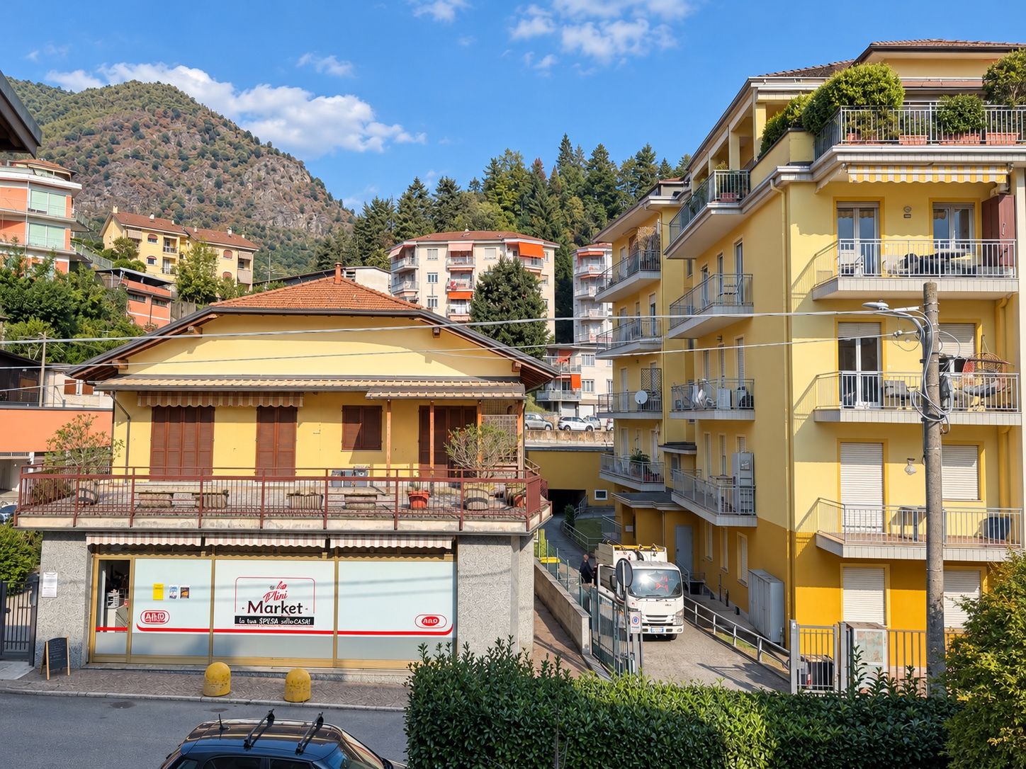 Un bâtiment jaune avec un balcon, une enseigne indiquant « Mini Market » et un camion garé.