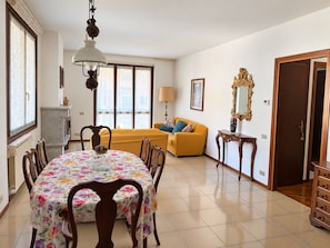 Un coin repas avec une table dressée pour quatre personnes, un canapé et un miroir au mur.