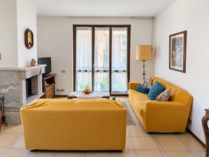 Ett vardagsrum med en soffa, ett soffbord, en öppen spis, en tv och ett fönster med gardiner.