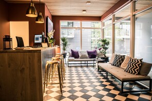 A modern interior with a checkered floor, a wooden reception desk, and a seating area with a sofa and chairs. - Welcome Apartments (Reykjavik)