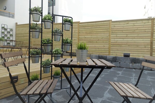 An outdoor seating area with wooden benches and tables, surrounded by metal planters with various plants. - Welcome Apartments (Reykjavik)