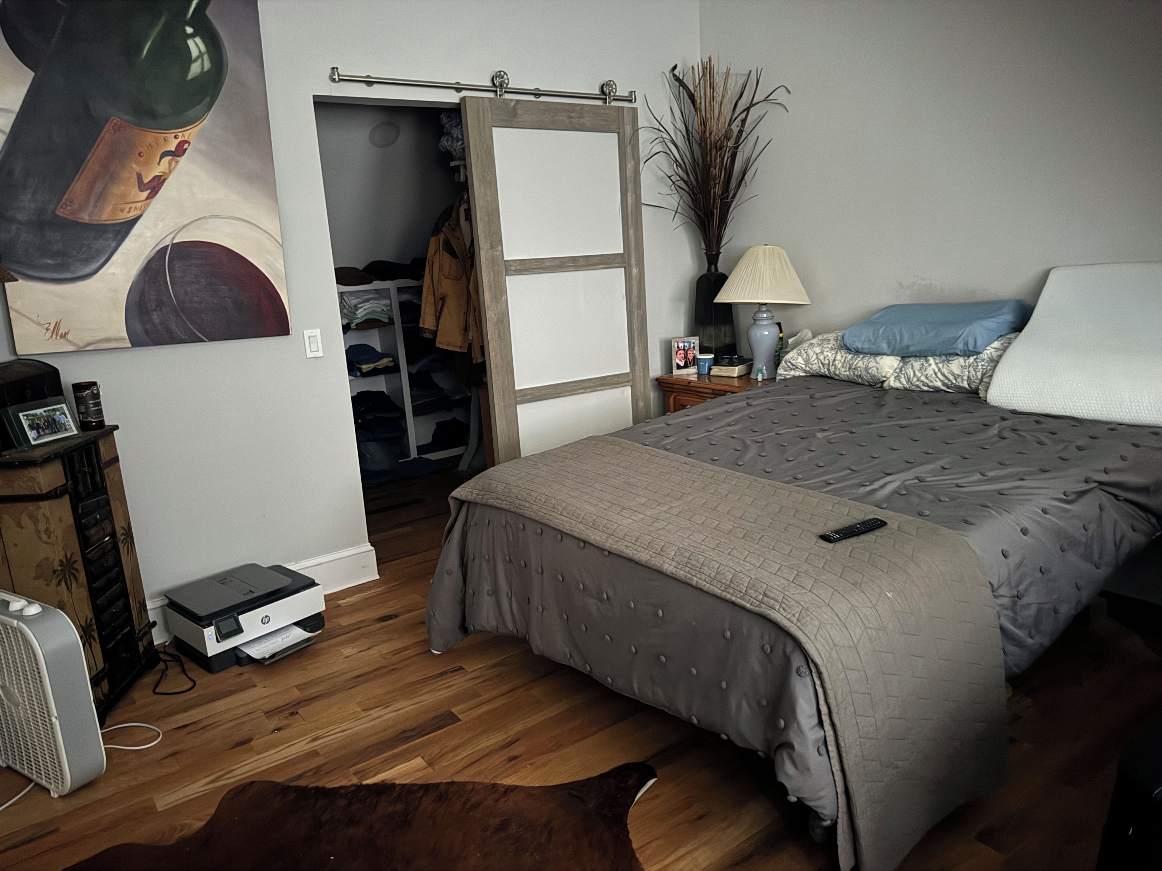 A bedroom with a bed, a bedside table, a lamp, a dresser, a fan, and a closet.