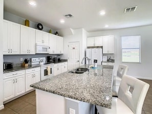 Una cocina moderna con gabinetes blancos, encimera de granito, microondas integrado y un lavamanos.