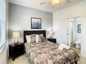 A bedroom with a bed, two bedside tables, a ceiling fan, a framed artwork above the bed, and a bathroom door in the background. - Family Oasis Near Disney - Pool & Resort (Davenport)