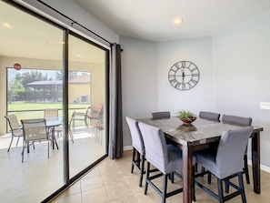 A dining area with a glass partition, a clock on the wall, and a view of the outdoors. - Family Oasis Near Disney - Pool & Resort (Davenport)