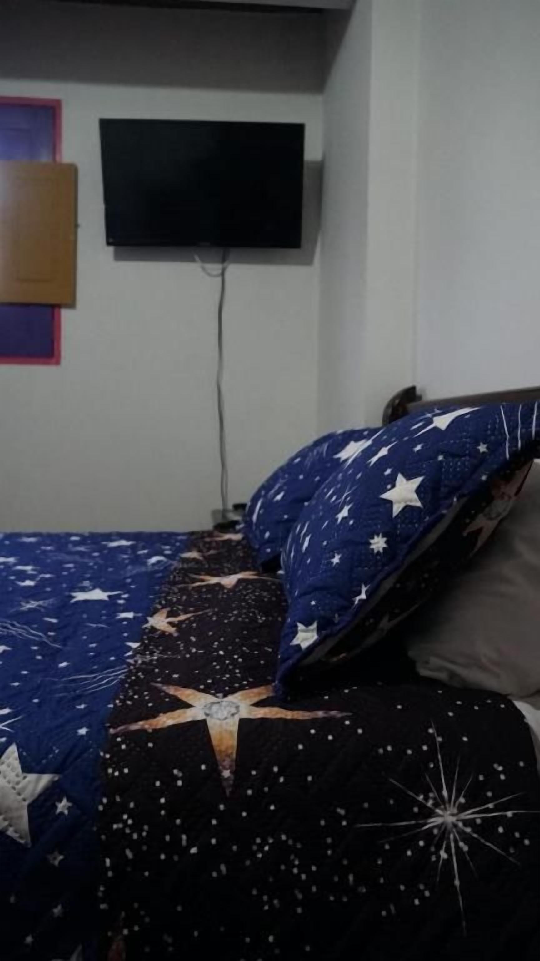 Un dormitorio con una cama, un televisor montado en la pared y una ventana.