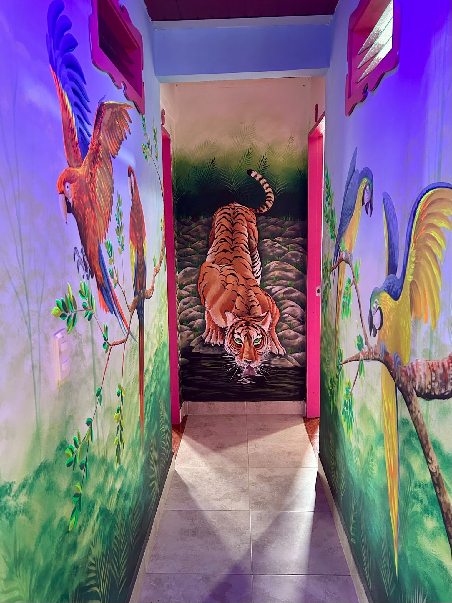 Un pasillo decorado con murales coloridos de fauna, incluyendo un tigre y aves, que conduce a una habitación.