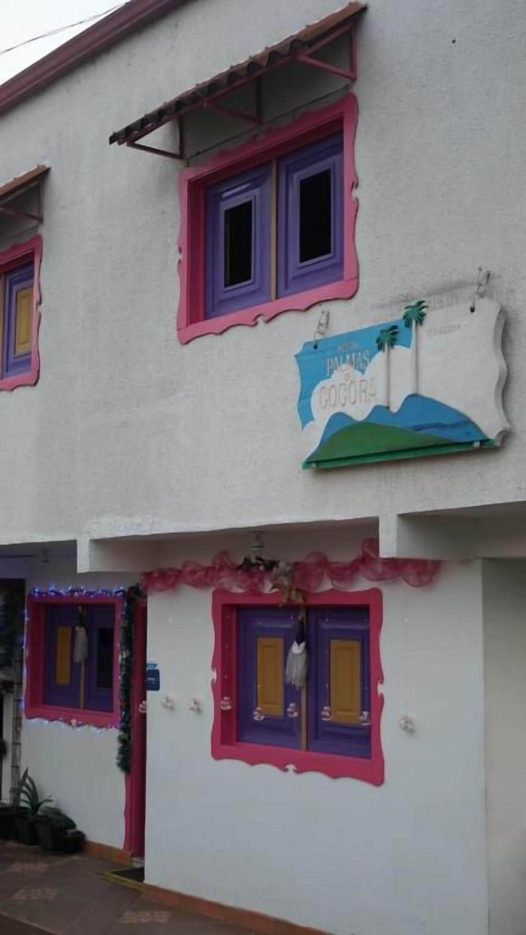 Un edificio con varias ventanas, algunas con contraventanas, y un letrero con una palmera y texto.
