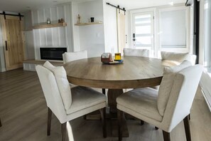 A round wooden dining table with six white upholstered chairs, a fireplace, and a sliding barn door.