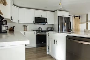 A modern kitchen with white cabinets, a microwave, a stove, a refrigerator, and a dishwasher.