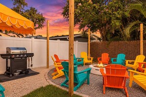 Un cortile con una griglia barbecue, poltrone Adirondack colorate e un braciere.