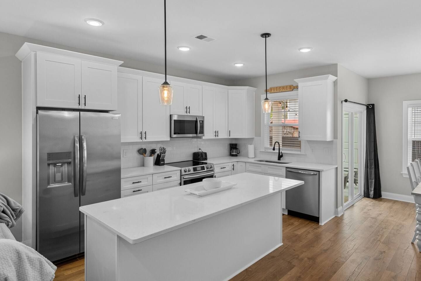 A modern kitchen with white cabinetry, stainless steel appliances, and pendant lighting.