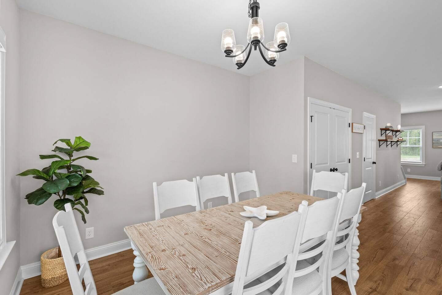 A dining area with a wooden table, white chairs, a chandelier, and a potted plant.