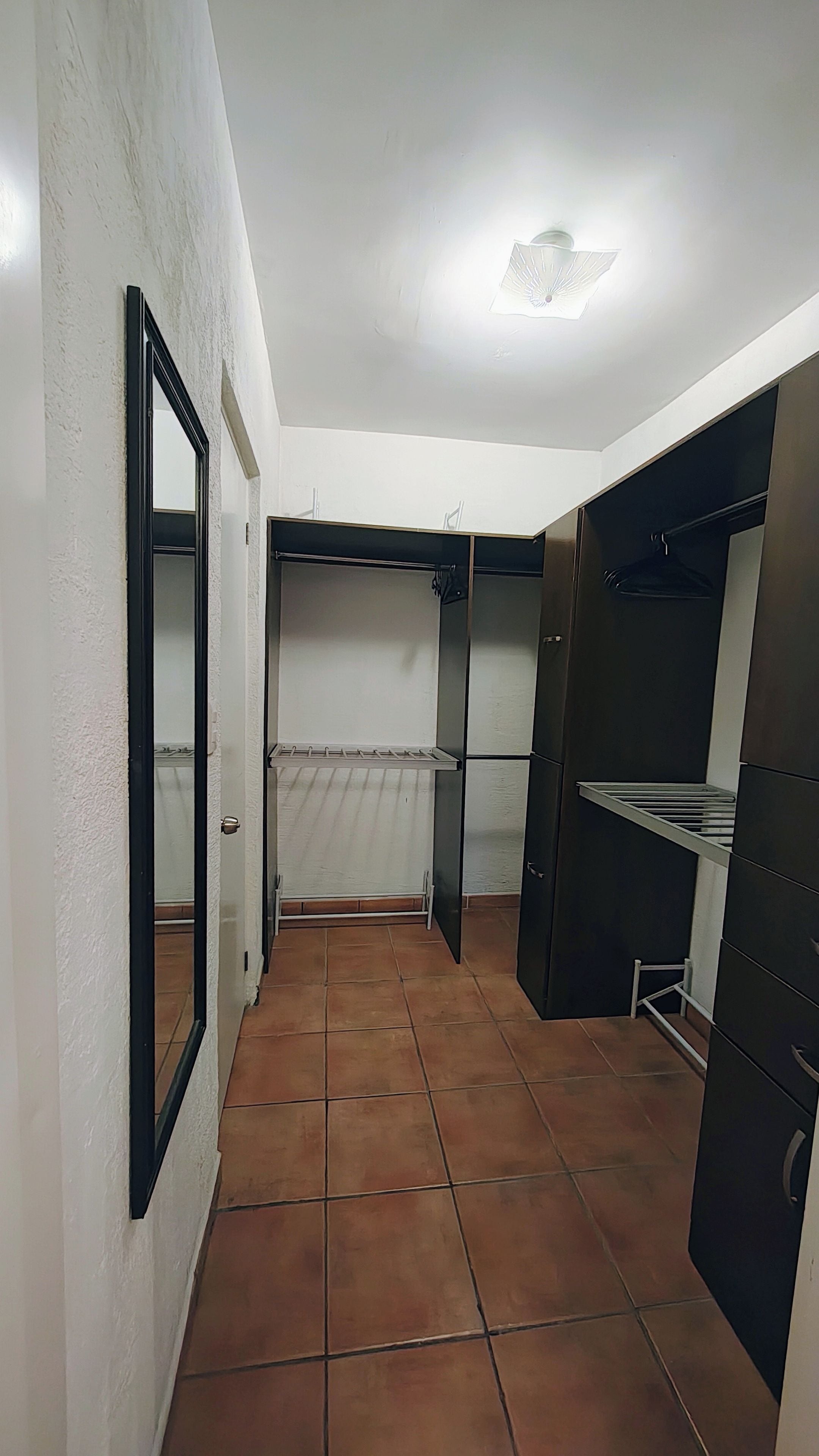 A narrow hallway with tiled flooring, a door on the left, and a closet with shelves on the right.