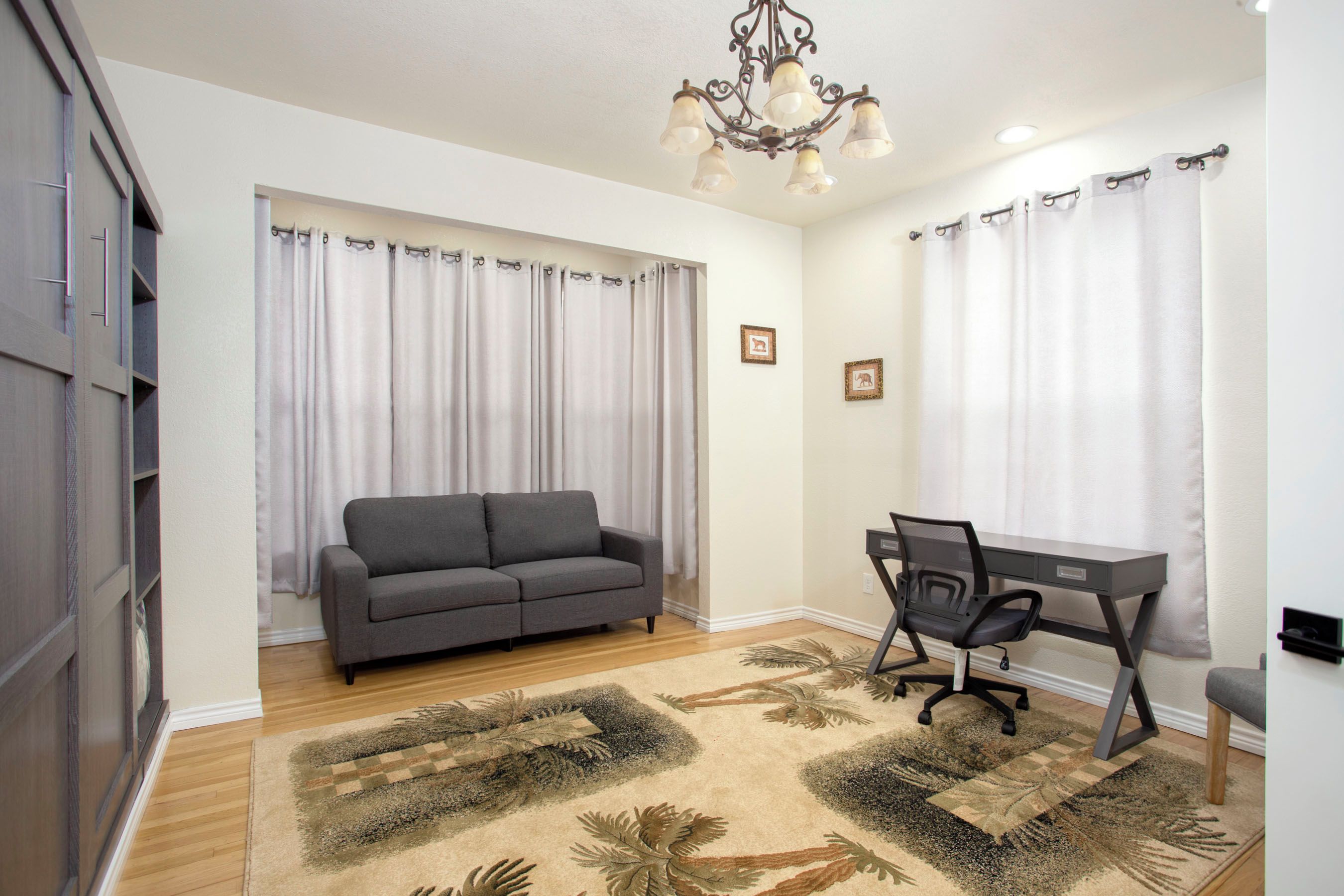 A modern living room with a grey sofa, a desk with a chair, and a chandelier.