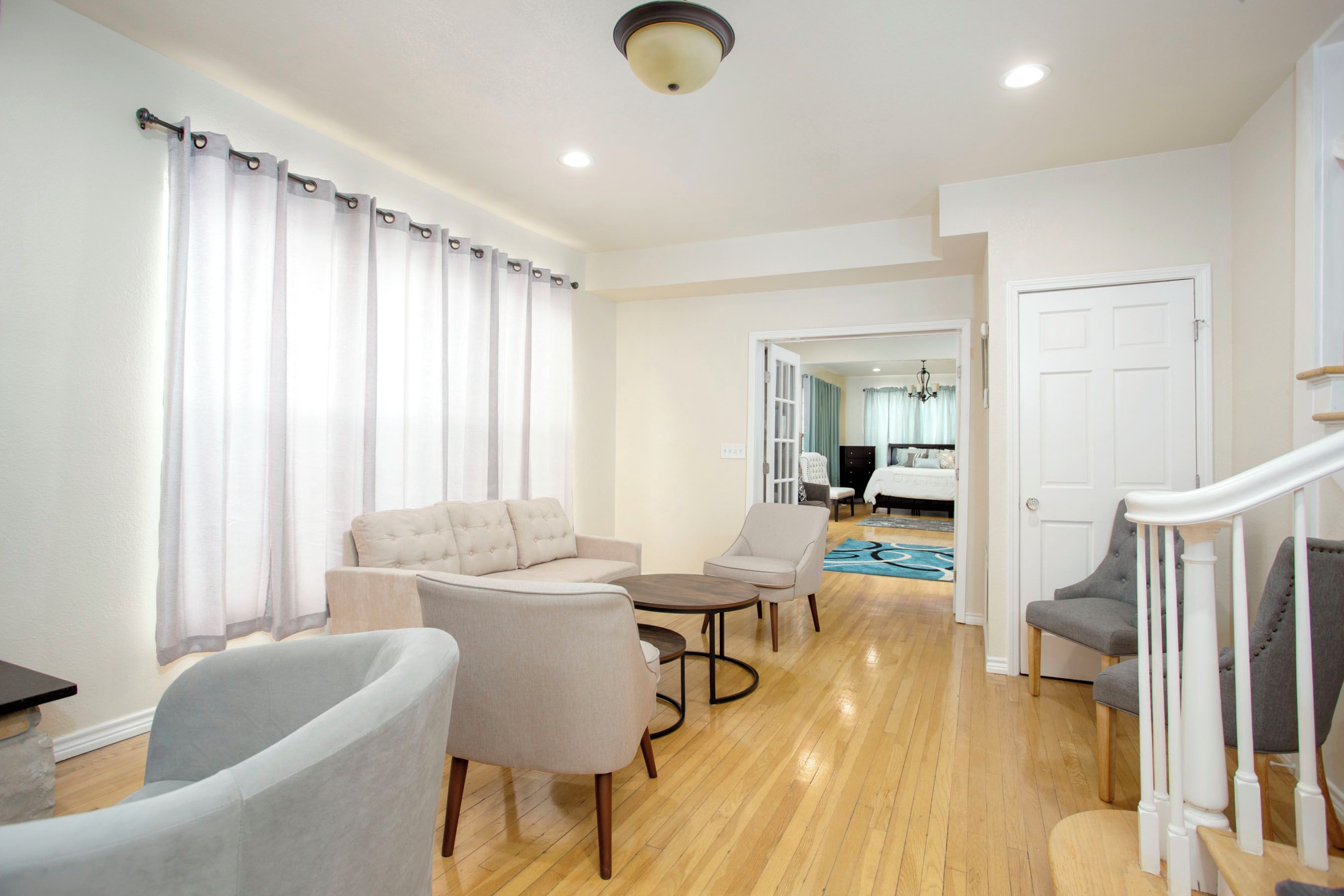 A spacious living area with a sofa, armchairs, and a coffee table. There is a staircase leading to another level, and a door to the right.