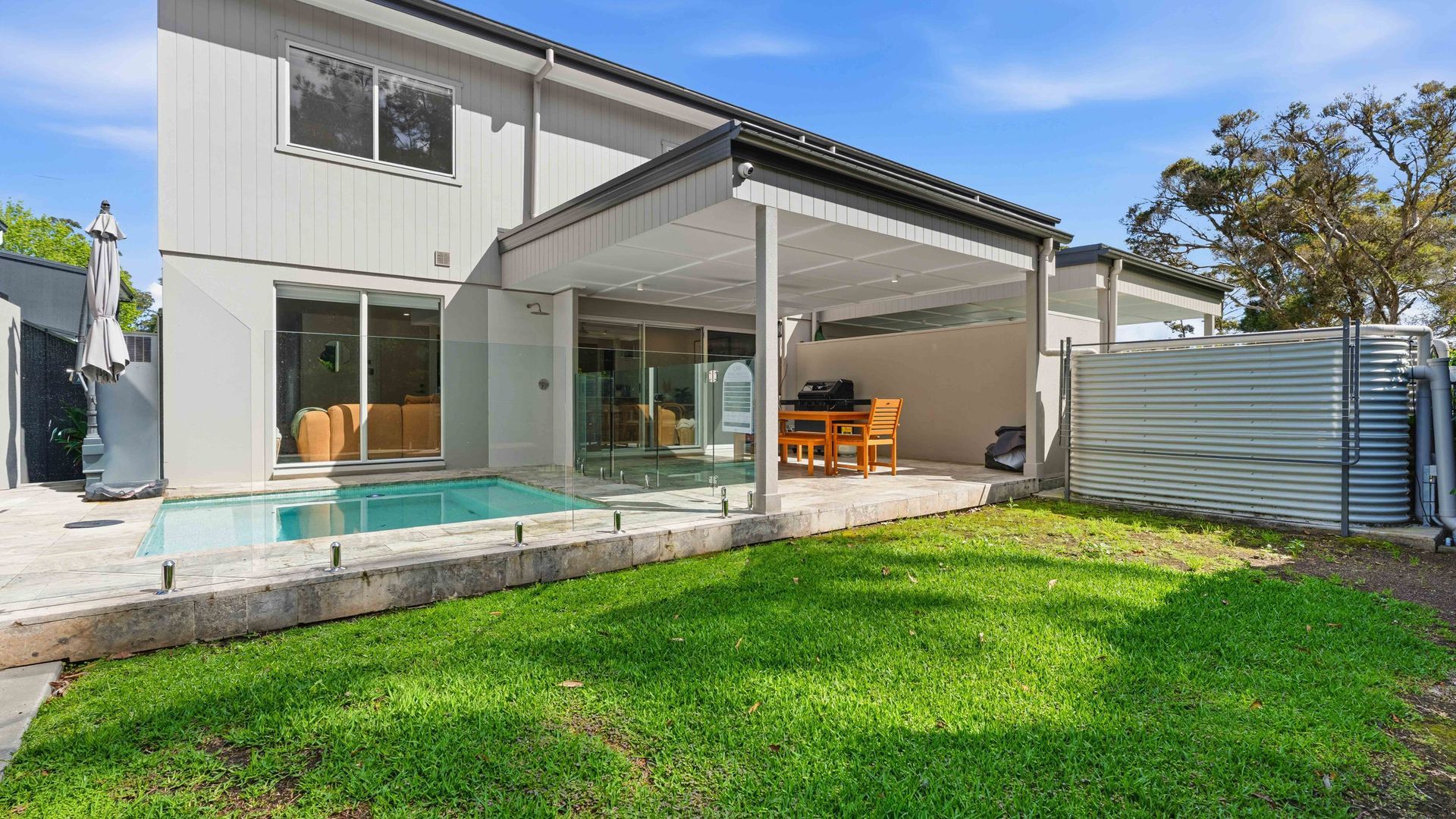A modern house with a covered patio, a swimming pool, and a well-maintained lawn.