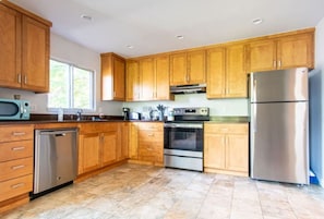 A modern kitchen with wooden cabinets, stainless steel appliances, and a dishwasher. - Panoramic Lake View 3800+ sqft House in Oasis (Seattle)