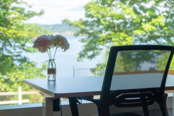 A table with a vase of flowers and a chair, overlooking a body of water and greenery. - Panoramic Lake View 3800+ sqft House in Oasis (Seattle)