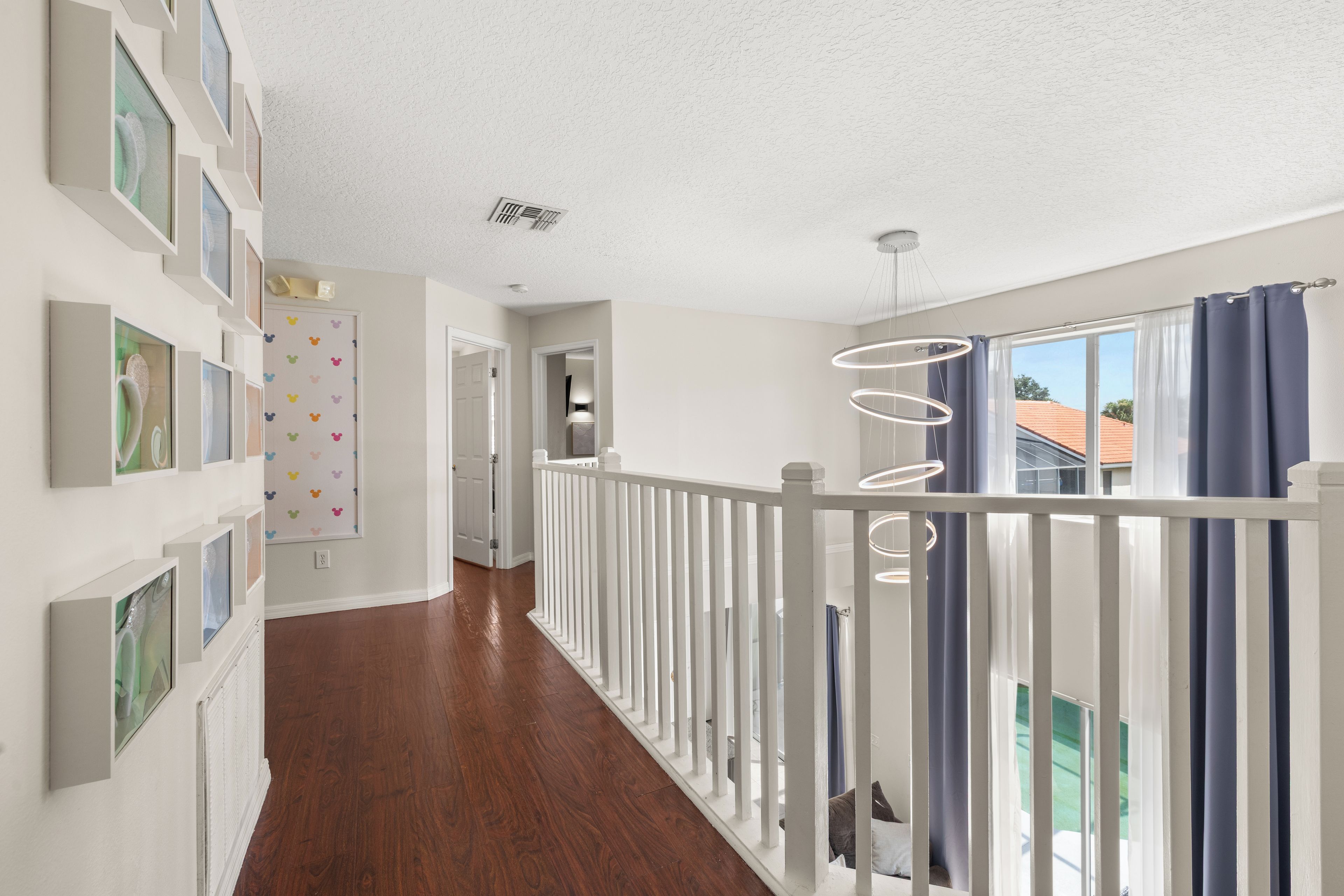 A hallway with a wooden floor, white walls, and a white railing.