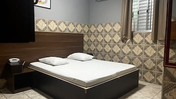 A bedroom with a bed, a nightstand, an air conditioning unit, and patterned tiles.