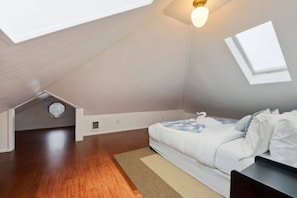 A room with a sloped ceiling, a bed with white bedding, a small window, and a ceiling light. - Spacious 4BR/2BA Home @Seattle | Ping Pong & BBQ (Seattle)