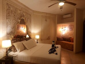 Ein Hotelzimmer mit einem großen Bett, zwei Nachttischlampen, einem Deckenventilator und dekorativen Wandverkleidungen.
